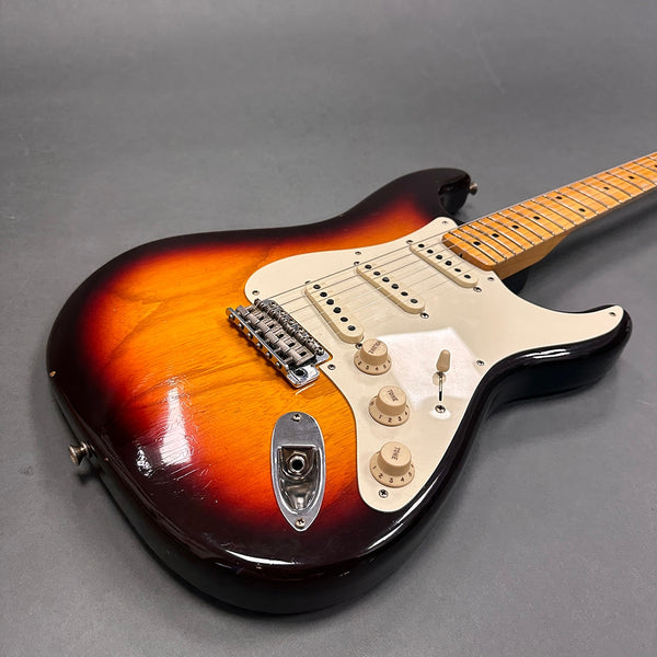 Vintage sunburst electric guitar with maple fretboard, white pickguard, and three single-coil pickups on gray background