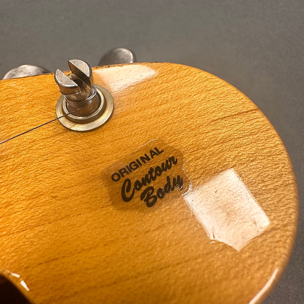 Close-up of guitar body showing Original Contour Body decal and strap button on natural wood finish