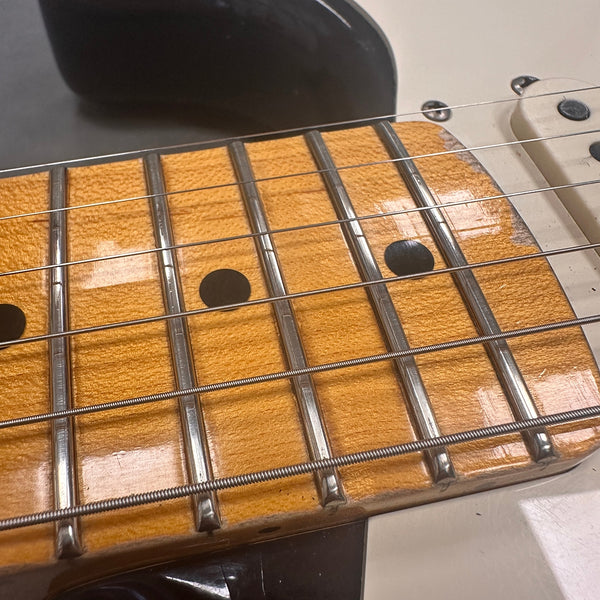 Close-up of electric guitar maple fretboard with metal frets and black dot inlays, steel guitar strings, white pickup, and cream-colored guitar body edge