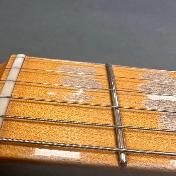 Close-up of worn guitar nut and strings on maple fretboard showing string grooves and metal fret wire