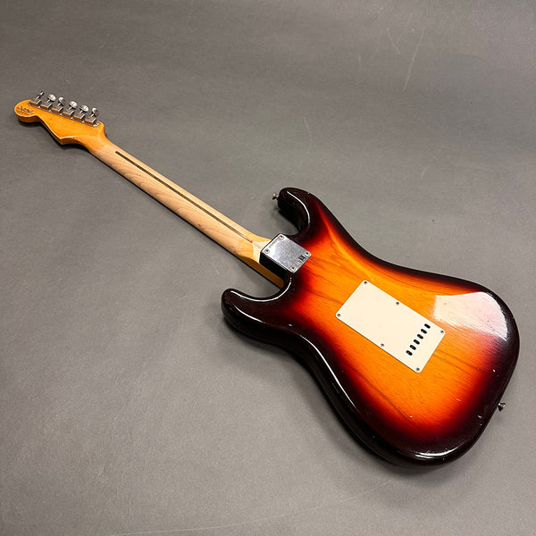 Back side view of sunburst electric guitar with maple neck and tuning pegs on gray background