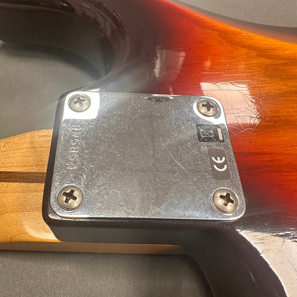 Close-up of electric guitar neck plate with serial number RG8948 and CE certification sticker on sunburst finish guitar body