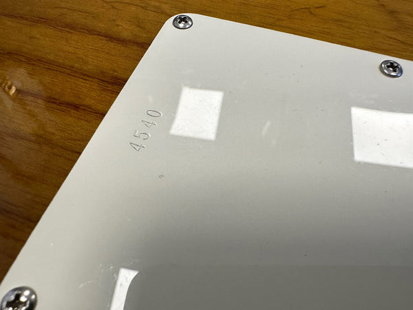 Close-up of white guitar backplate on wood body with serial number 4540 engraved near corner screws