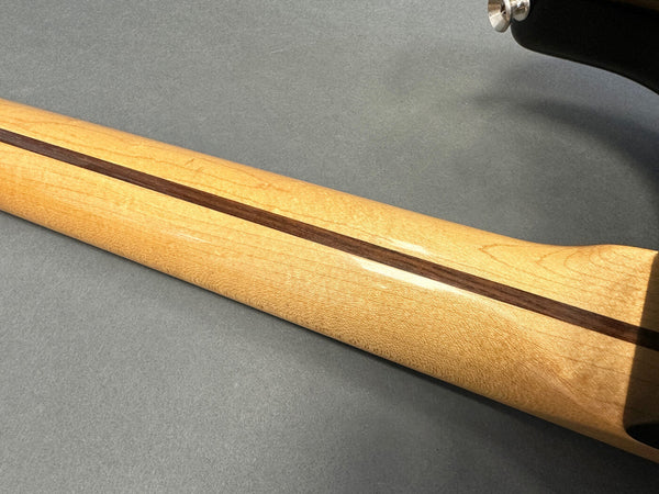 Close-up of a maple guitar neck with a walnut skunk stripe and a portion of the guitar headstock on a gray background