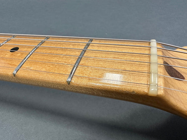 Close-up of natural wood guitar neck and fretboard with metal frets and six guitar strings, showing nut and first frets on gray background