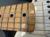 Close-up of electric guitar maple fretboard with metal frets and black dot inlays, showing steel strings and part of white guitar body.