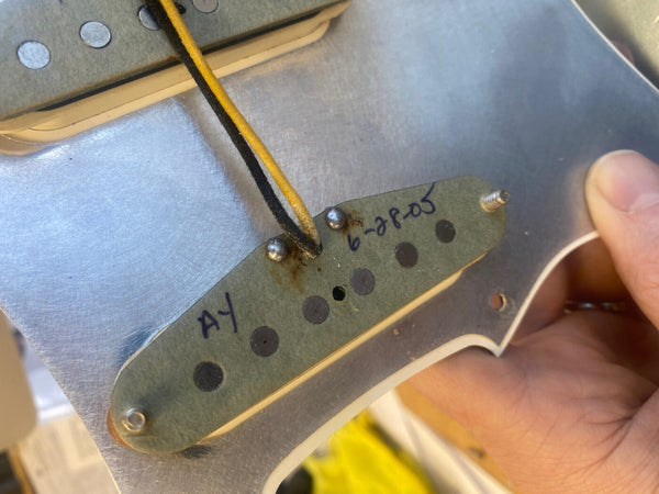 Close-up of vintage single-coil guitar pickup with yellow and black wires mounted on metal guitar pickguard, dated 6-28-05 handwritten on pickup baseplate.