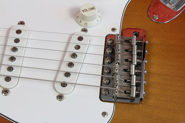 Close-up of electric guitar bridge, volume knob, and white single-coil pickups on a brown body guitar
