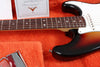 Close-up of Fender Custom Shop electric guitar with rosewood fretboard and sunburst finish on orange plush case lining, showing certificate of authenticity