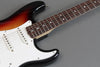 Close-up of sunburst electric guitar body and fretboard with white pickguard and single coil pickups on gray background