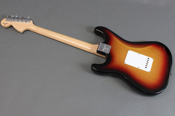 Back of Fender Stratocaster electric guitar in sunburst finish with maple neck and white tremolo cavity cover on gray background