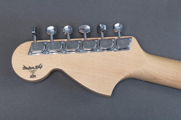 Close-up of maple wood electric guitar headstock with six chrome tuning pegs and Custom Shop USA logo on gray background