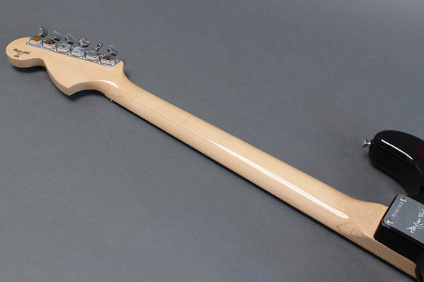 Back view of electric guitar with light wood neck and chrome tuning pegs on gray background