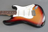 Sunburst electric guitar with white pickguard, rosewood fretboard, and three single-coil pickups on gray background
