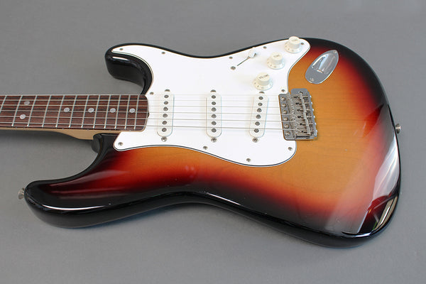 Electric guitar with sunburst finish, white pickguard, three single-coil pickups, and rosewood fingerboard on gray background