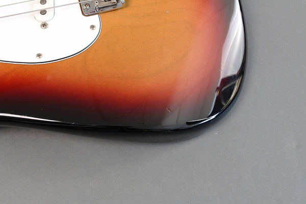 Close-up of sunburst finish electric guitar body corner with visible scratches and dings on grey background