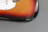 Close-up of sunburst finish electric guitar body with white pickguard and metal bridge on gray background
