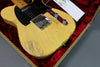 Vintage worn yellow electric guitar with black pickguard inside red velvet lined case, close-up view of body and controls