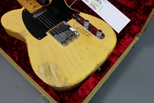 Vintage worn yellow electric guitar with black pickguard inside red velvet lined case, close-up view of body and controls