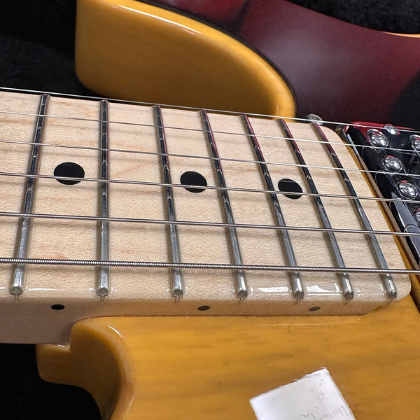 Close-up of maple guitar fretboard with black dot inlays and six strings on a natural wood electric guitar body
