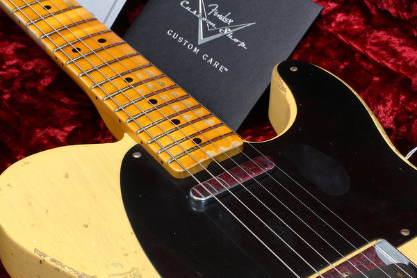 Close-up of vintage Fender Telecaster electric guitar with worn butterscotch blonde finish and maple neck on red velvet background with Fender Custom Shop Custom Care booklet