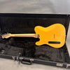 Back view of Fender electric guitar with natural wood finish inside black plush-lined hard case on gray background