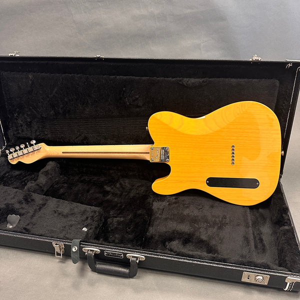 Back view of Fender electric guitar with natural wood finish inside black plush-lined hard case on gray background