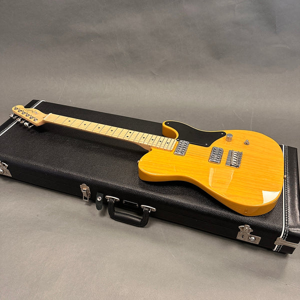 Electric guitar with natural wood finish and black pickguard lying on closed black guitar case against gray background