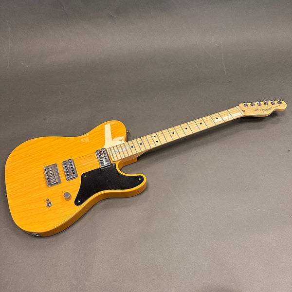 Fender electric guitar with natural wood finish, maple neck, black pickguard, and dual humbucker pickups on gray background