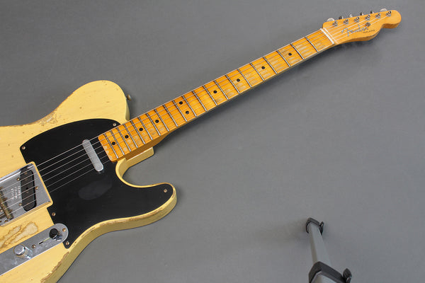 Vintage Fender Telecaster electric guitar with worn yellow finish and black pickguard on gray background