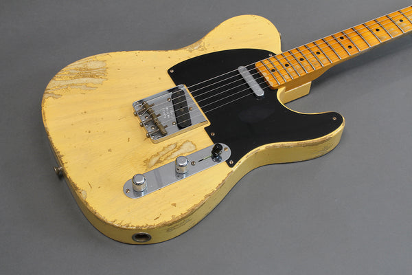 Vintage distressed yellow electric guitar with black pickguard and maple fretboard on gray background