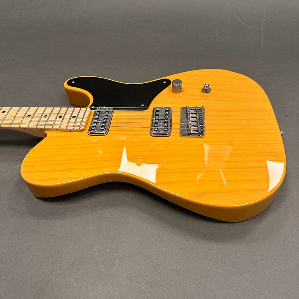 Electric guitar with natural wood finish, black pickguard, dual humbucker pickups, maple neck, and chrome hardware on gray background
