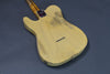 Vintage yellow electric guitar body with worn finish and string ferrules on dark gray background