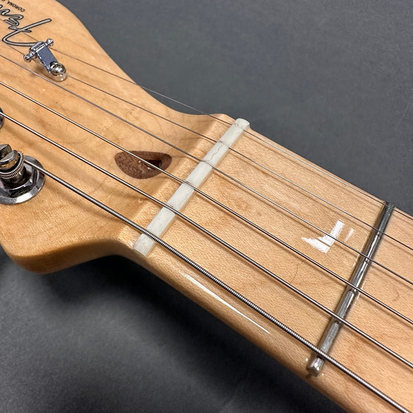 Close-up of Fender guitar headstock showing tuning peg, nut, strings, and maple fretboard with glossy finish on dark background