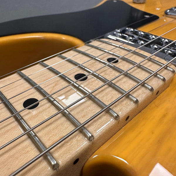 Close-up detail of electric guitar maple fretboard with metal frets and steel strings on honey-colored body
