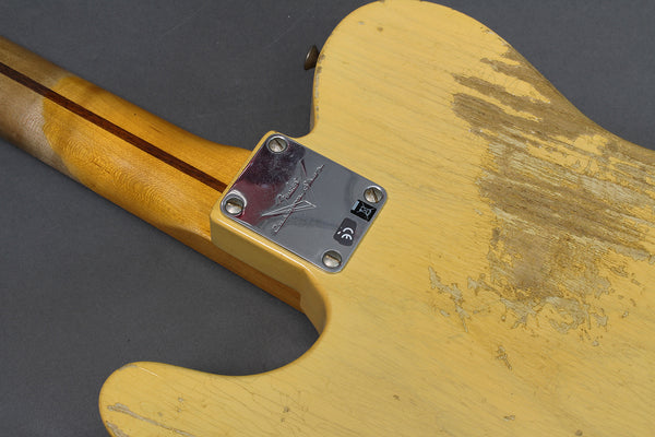 Close-up of worn vintage yellow electric guitar body and neck with metal Fender Custom Shop neck plate and relic finish detailing