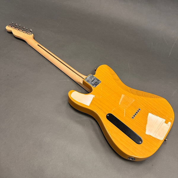 Back view of a Fender electric guitar with a glossy honey blonde finish and a light maple neck on a gray background