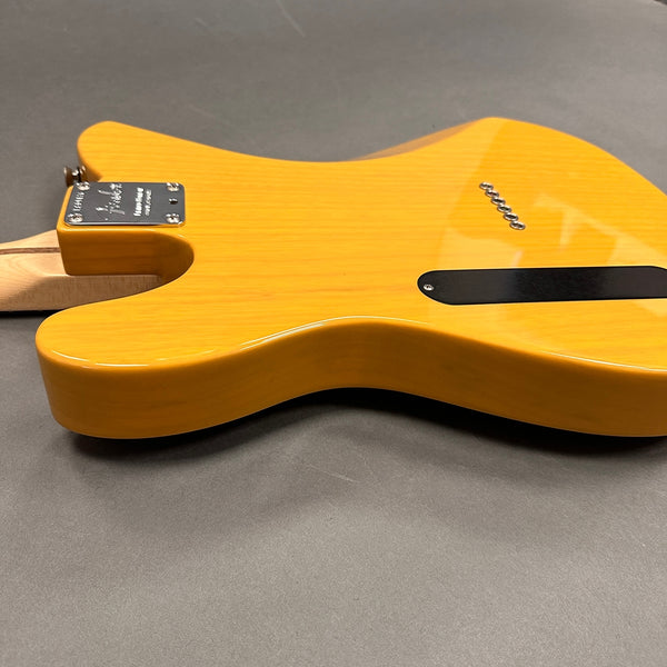Back view of yellow electric guitar body with maple neck and chrome neck plate on gray surface