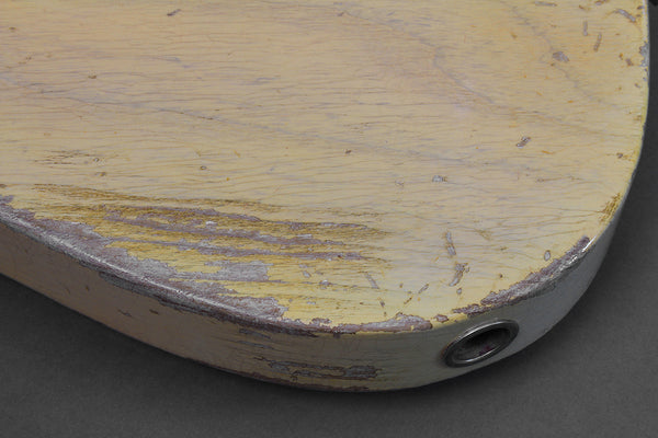 Close-up of worn and chipped yellow guitar body edge with visible wood grain and input jack hole