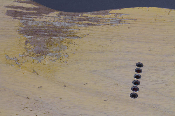 Close-up of vintage guitar body finish with worn and cracked yellow paint and six string ferrules, showcasing relic aged detailing