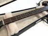 Close-up of electric bass guitar neck and fretboard with metal strings inside plush lined black guitar case with silver latch on white background