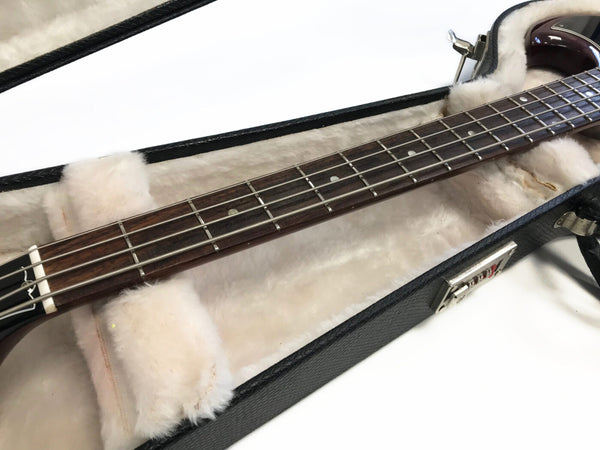 Close-up of electric bass guitar neck and fretboard with metal strings inside plush lined black guitar case with silver latch on white background