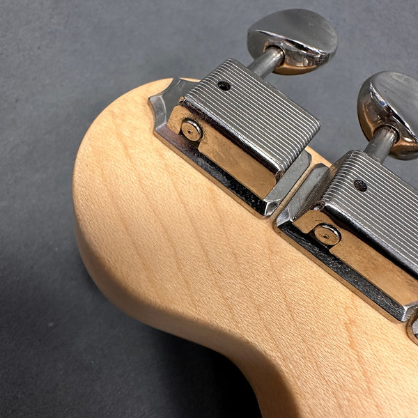 Close-up of chrome tuning pegs and natural wood guitar headstock on dark background