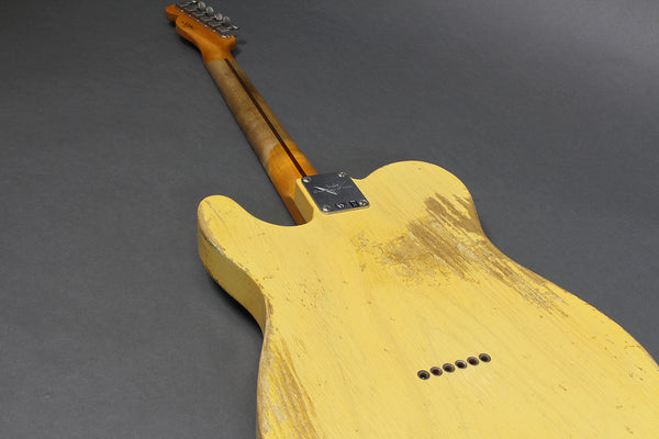 Vintage yellow electric guitar with worn finish and bolt-on maple neck, back view against gray background