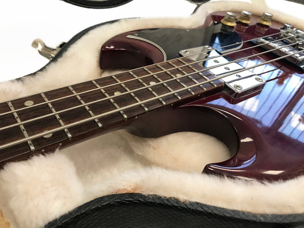 Close-up of cherry red electric bass guitar neck and body with chrome pickups resting in a plush white fur-lined guitar case