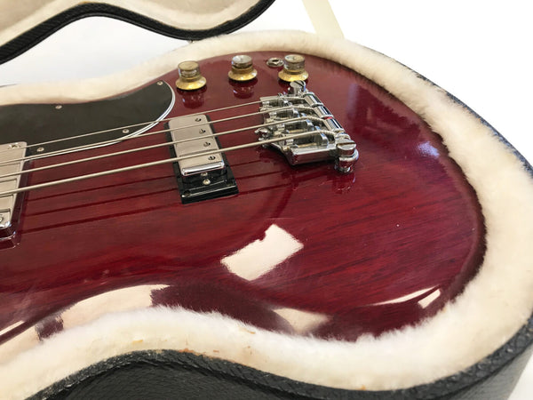 Close-up image of cherry red electric bass guitar body with chrome bridge and pickups in plush-lined guitar case.