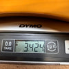 Close-up of a DYMO digital scale display showing a weight measurement of 3.424 kilograms, used for weighing guitar-related items at Coffee House Guitars.