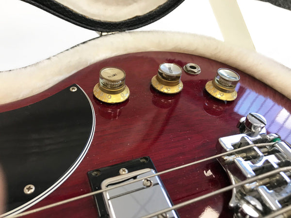 Close-up of volume knobs and bridge on red electric guitar in plush-lined guitar case