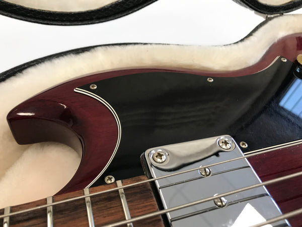 Close-up of cherry red electric guitar body with black pickguard and chrome pickup in guitar case with plush white lining