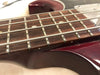 Close-up of rosewood fretboard with metal frets and nickel strings on a dark red electric bass guitar body